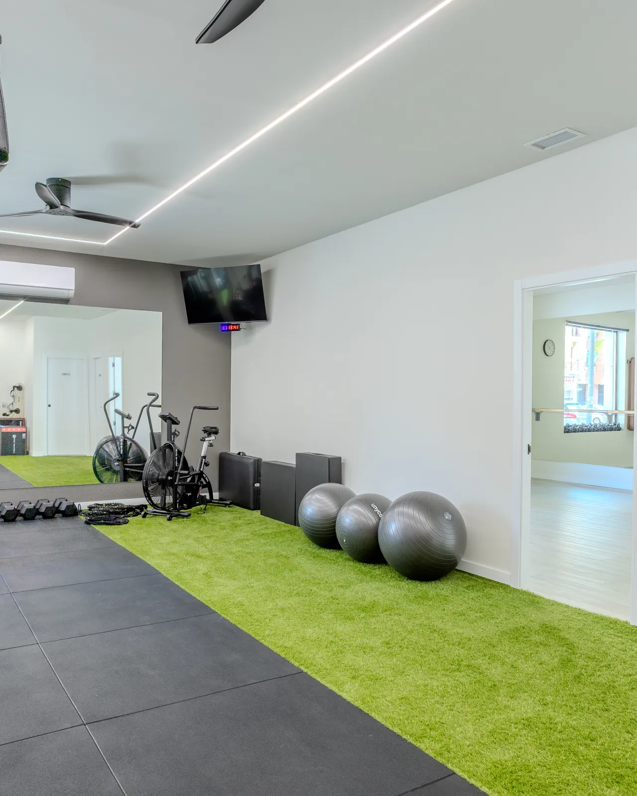 Sala de entrenamiento vista hacia el espejo, con bicicleta de aire y fitballs sobre césped artificial
