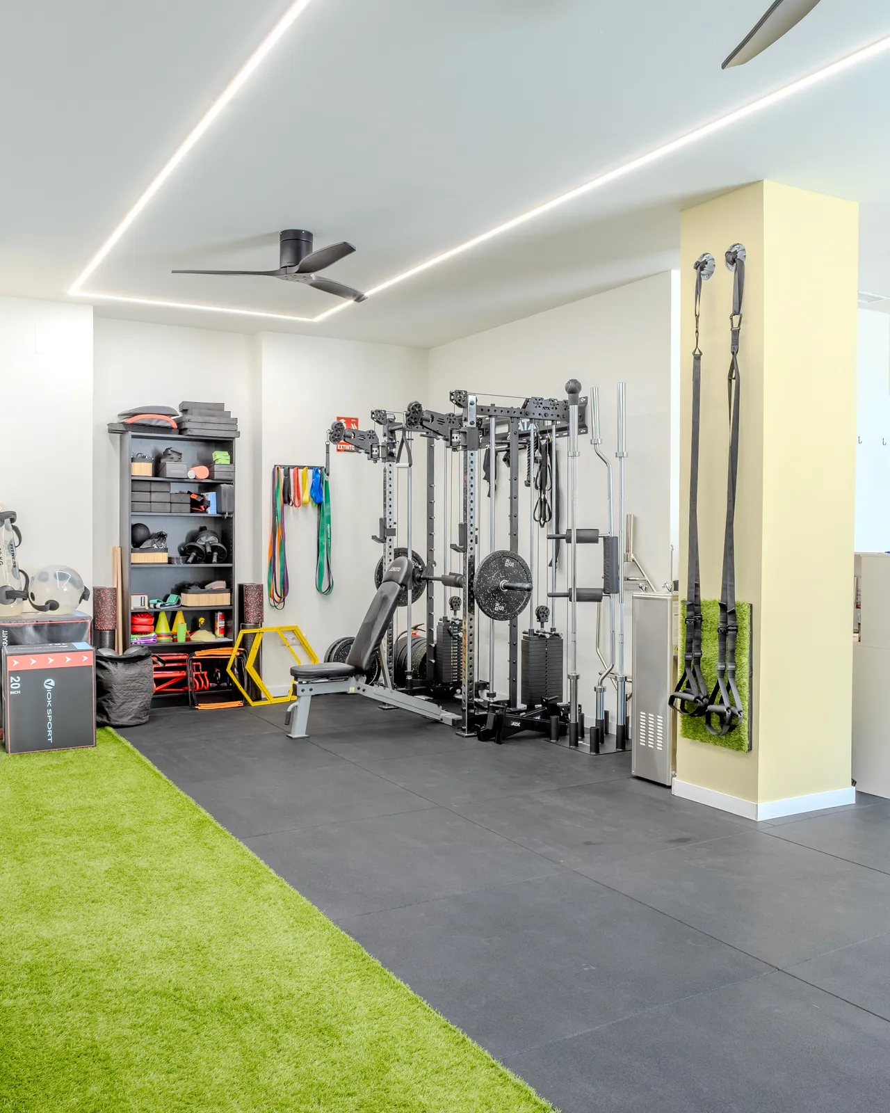 Sala de entrenamiento con rack multiestación, estantería de material y una franja de césped artificial
